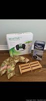 Photo showing all four items: boxed Revitive IX Circulation Booster, boxed Foot Rocker, wooden foot roller, and bean bag sack with floral design.