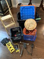 Overview of the garage package including wooden 2-step ladder, storage bins with blue lids, orange extension cord, black crates with tools, and decorative sun piece