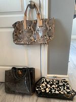 Three handbags displayed together: Cole Haan taupe snake skin tote hanging on knob, Karen Wilson black and white bag with plastic bottom and silver clip closure, and medium grey snake skin leather handbag