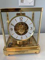 Front view of brass and glass mantel clock with white dial and exposed movement