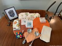 Photo showing a curated group of peach-colored placemats, napkins, cloth coasters, eclectic frog candlesticks, small acorn art piece, and decorative cloth items featuring various animal and floral motifs on a wood table.