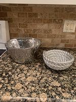 Both decorative silver bowls shown side by side on kitchen counter with stone tile backsplash.