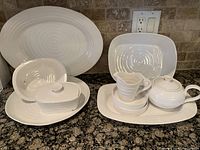 Full assortment of white ceramic serving pieces arranged on countertop, showing all shapes and counts.