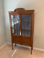 Front view of closed vintage wood china cabinet with glass panel doors and brass key tassel lock.