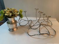 Wide angle shot showing 5 wavy silver candle sticks and a pewter-look pitcher with faux greenery