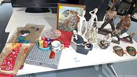 Image showing multiple statues, silk panels, framed tiger print, small fan, stones, sake cups, tea cup, and other collectibles on a white table.