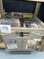 Large storage bin filled with approximately 43 music CDs in jewel cases showing various album covers and artists, arranged in shelves.