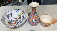 Photo showing the ceramic bowl, vase, and breakfast mug on a table, highlighting the colorful fish patterns and overall shapes