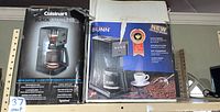 Boxes of a Cuisinart Brew Central 12-cup coffee maker and a Bunn 10-cup coffee maker on a shelf.