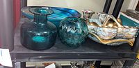 Shelf showing blue crackle glass bottle, blue cut glass votive holder, and a blue and gold decorative dish with an abstract shape.