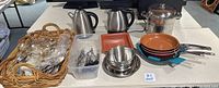 Wide view of the entire lot showing all items together on a table including basket of silverware, scissors bin, kettles, pans.