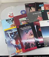 Photo of LaserDisc collection spread on a table showing a mix of movie and music titles with some discs in white protective sleeves.