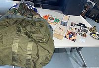 Overview photo showing the camouflage field jacket, two green mobility bags, and some flags and memorabilia on a table.