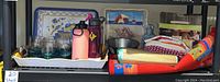 Shelf with plastic dishes, water bottles, cloth items including beach mat and scatter rug, galvanized lantern, metal and plastic serving trays