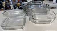 Stacked clear glass baking dishes showing rectangular and square shapes with handles, including multiple of the same size and some loaf pans.