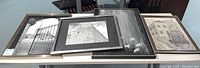 Four framed black and white photo prints and canvas art pieces laid out showing variety of scenes including architecture and people in rain.