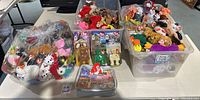 Large assortment of assorted TY Beanie Babies plush toys and packaging displayed in bins and plastic bags on table.
