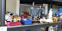 Shelf with novelty banks shaped as dogs, various glass and ceramic figures, and decorative containers with some brass items in background.