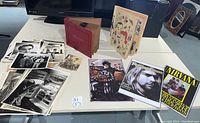 Photo showing a table with a red scrapbook, a colorful illustrated scrapbook, several black and white posters including Nirvana and Kurt Cobain, Edward Scissorhands or Beetlejuice poster, and vintage 78rpm records