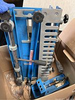 Blue Kreg Rip-Cut jig with knobs and clamps in cardboard box with a metal handle and other tool parts visible.