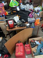 Wide view of assorted automotive supplies on table and floor, showing inflator, pumps, charger, gas cans and various tools and boxes.
