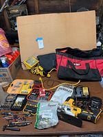 Full view of the lot showing DeWalt cordless jigsaw, bit sets, charger, and portable work light on table with cardboard backdrop