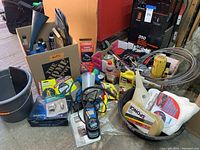 Overall lot view showing various automotive supplies including oils, tools, and cleaning items next to a Solar 350 battery charger booster and coiled wire rope.