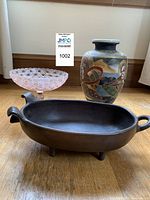 Three primary items on wooden floor: Satsuma-style vase, pink pedestal candy dish, and pig casserole dish