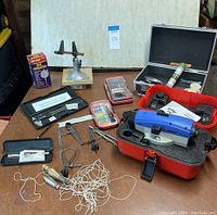 Wide view of all drafting, measurement, and leveling tools on table including carrying cases and various small instruments.