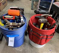 Two buckets—one blue plastic bucket with assorted tools including hammers and rollers, and one white bucket with red fabric sleeve holding hammers and pliers