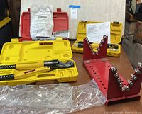 Image showing the yellow hydraulic pliers in case, the red metal pipe threading die holder, and two yellow cases with hydraulic steel bar cutter parts.