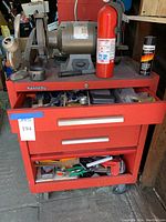Bench grinder mounted on top of red Kennedy tool box, with fire extinguisher and lubricant can on surface