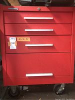 Front view showing three drawers and bottom drawer with silver handles, red textured paint, Kennedy brand badge and locking casters visible at bottom