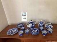 Full view of the tea service laid out on a wooden surface showing teapot, pitchers, cups, saucers, and plates, all blue and white ceramic with detailed patterns.