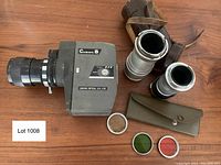 Front angled view of the Crown 8 EZS camera with zoom lens, two silver Leitz lenses, and three colored filters (green, red, clear) laid out on table.