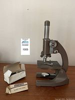 Side angle view of the Swift monocular microscope with slides and dropper boxes on table.