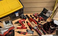Overview of assorted Milwaukee red and black corded and cordless tool bodies on wooden surface with storage bin and tool bag.