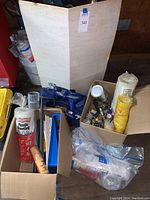 Overview of lot contents showing plastic sheeting rolls, trays, paint tools and dropcloth in boxes