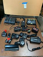 Entire lot laid out on table showing multiple battery chargers, power supplies, and rechargeable batteries from Ryobi and DeWalt.