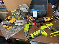 Wide view of all power tools and accessories on table including DeWalt and Ryobi branded tools, and drill bits in packaging.