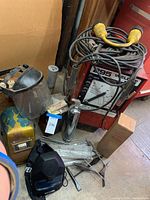 Wide view showing 295 model rod welder machine with power cables and connectors, assorted welding rods, YES Welder protective helmet, small hammers, and two metal fire extinguishers.