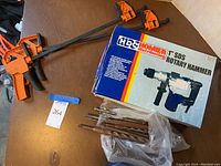 Rotary hammer box, two orange bar clamps, and a plastic bag with assorted drill bits.