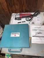 Makita cordless drill in blue carrying case, red and black oscillating multitool with accessories and manuals