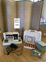 Photo showing Kenmore 3204FB sewing machine with power cord, case, stitch pattern discs, box of bobbins, metal accessories box, folding sewing pattern guide and vintage wood hem ruler.