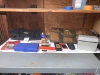 Full lot displayed on white table showing all items including pouches, boxes, sharpening stone, various tools, and bags.