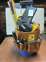 Front view of the wheelie bucket filled with assorted hand tools including chisels, large screwdrivers, a Minwax blend-fill pencil, tape measure, and a Channellock pouch.