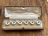 Six buttons in original hinged box, box open on wood surface