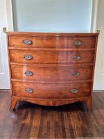 Front view showing full bow-shaped profile, four graduated drawers and brass bail handles.