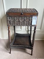 Full front view of antique wicker sewing stand with hinged lid and lower shelf, showing overall shape and condition.