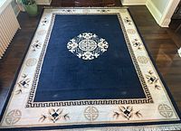 Full view of blue and cream wool rug with gold accents and central medallion on hardwood floor, showing overall condition and pattern